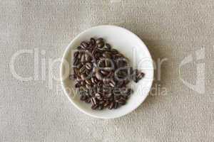 Fresh whole coffee beans inside of a small white saucer