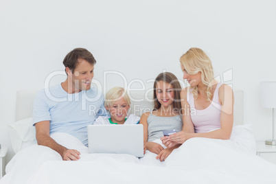 Family sitting in bed and using a laptop