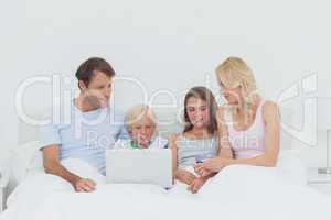 Family sitting in bed and using a laptop