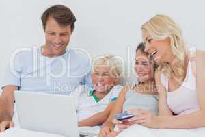 Family using computer and credit card in bed