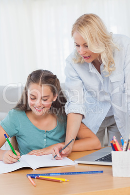 Little girl writing on a book while her mother is helping her