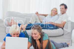 Children using a laptop lying on a carpet