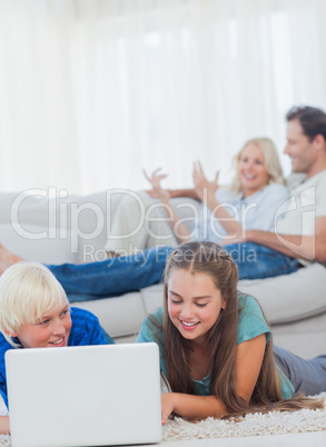 Siblings using a laptop lying on a carpet