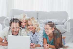 Beautiful family using a laptop lying on a carpet