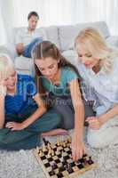 Siblings and mother playing chess sitting on a carpet
