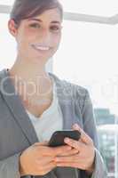 Businesswoman texting on smartphone and smiling at camera