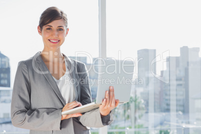 Businesswoman holding laptop and smiling at camera