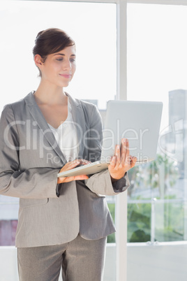 Smiling businesswoman holding laptop and standing