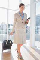 Businesswoman pulling her suitcase and checking her phone