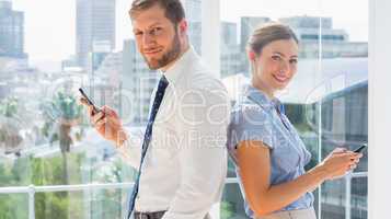 Smiling business team standing back to back and texting