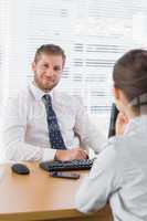 Businessman smiling with a co worker sitting at his desk