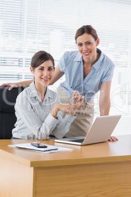 Happy businesswomen at desk smiling at camera