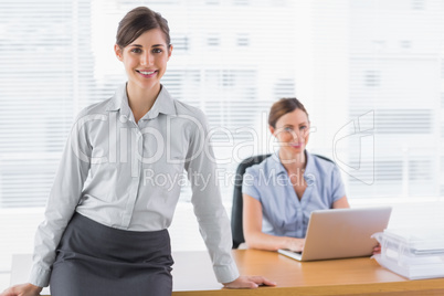 Businesswomen smiling at camera with one standing and one sittin
