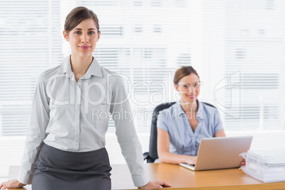 Businesswomen smiling at camera with one sitting and one standin