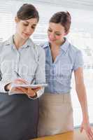 Businesswoman watching her co worker write on clipboard