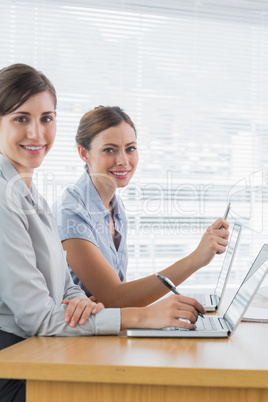 Smiling businesswomen working on their laptops portrait