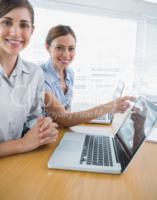 Businesswoman pointing to something on laptop for colleague port