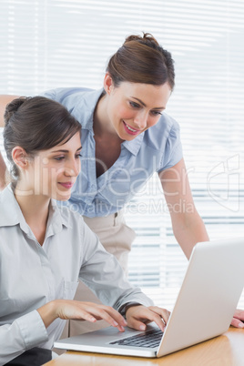 Businesswoman leaning over to look at colleagues laptop