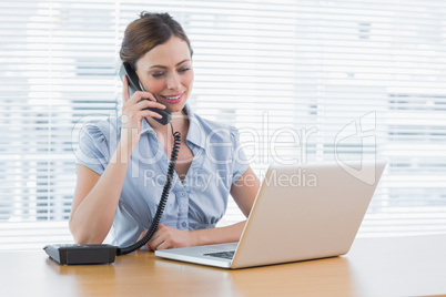 Businesswoman phoning and looking at laptop