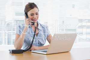 Businesswoman phoning and looking at laptop