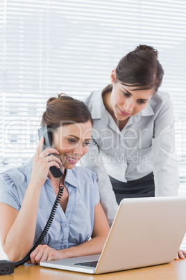 Businesswoman phoning and looking at laptop with colleague