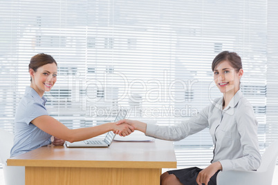 Businesswoman shaking hands with interviewee and both smiling at