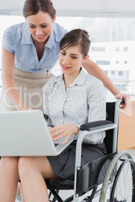 Businesswoman looking at co workers laptop who is sitting in whe