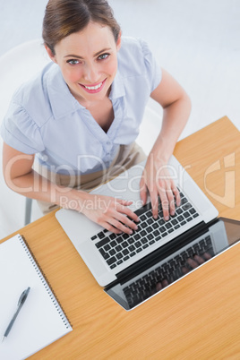 Businesswoman typing on her laptop and smiling up at camera