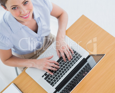 Pretty businesswoman typing on her laptop and smiling up at came