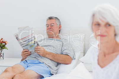 Mature man reading a newspaper in bed