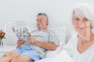 Mature man reading a newspaper in bed