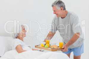 Mature man bringing wife breakfast in bed