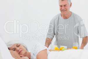 Mature man bringing sleeping wife breakfast in bed
