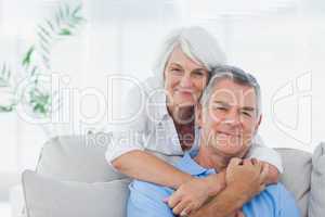 Woman embracing husband who is sitting on the couch
