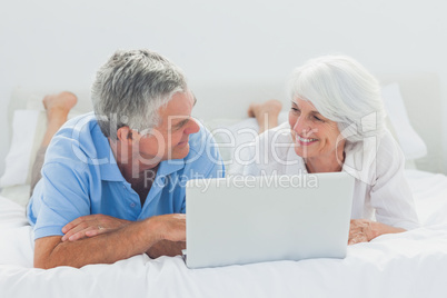 Couple lying and using a laptop pc in bed