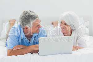 Couple lying and using a laptop pc in bed