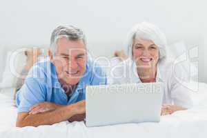 Couple lying and using a laptop in bed