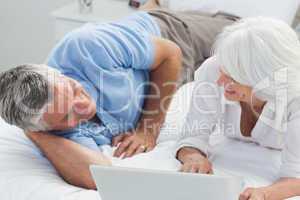 Couple lying in bed and using a laptop