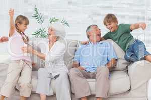 Grandchildren jumping on couch with their grandparents