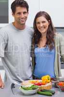 Cheerful couple smiling at camera and preparing vegetables