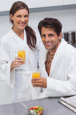 Lovely couple wearing bathrobes and holding glass of orange juic