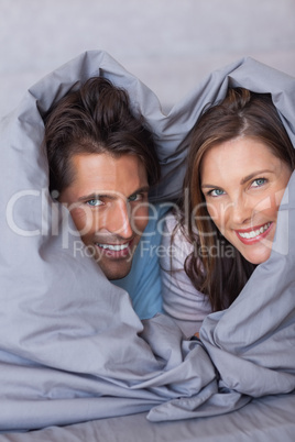 Delighted couple having fun wrapped in their duvet