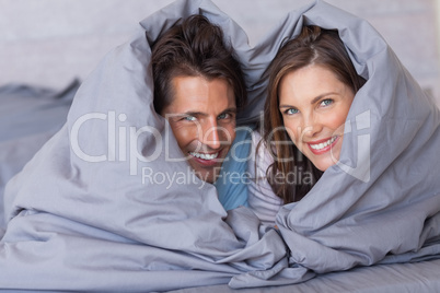 Smiling couple having fun wrapped in their duvet