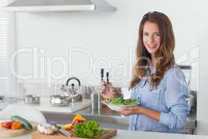 Woman in the kitchen holding a salad bowl with lettuce