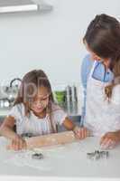 Little girl spreading a dough with a rolling spin