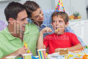 Little boy eating a birthday cake with parents