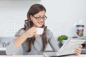 Woman holding a cup of coffee and reading a newspaper