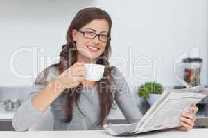 Woman holding a cup of coffee while reading a newspaper