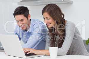 Happy couple using a laptop in the kitchen