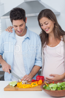 Pregnant woman looking at husband cutting vegetables